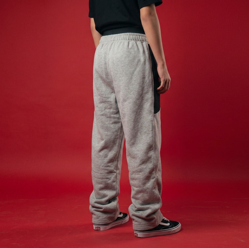 A person shown from the back wearing light heather gray sweatpants with black side panels, a black t-shirt, and black low-top sneakers, set against a solid red studio background.