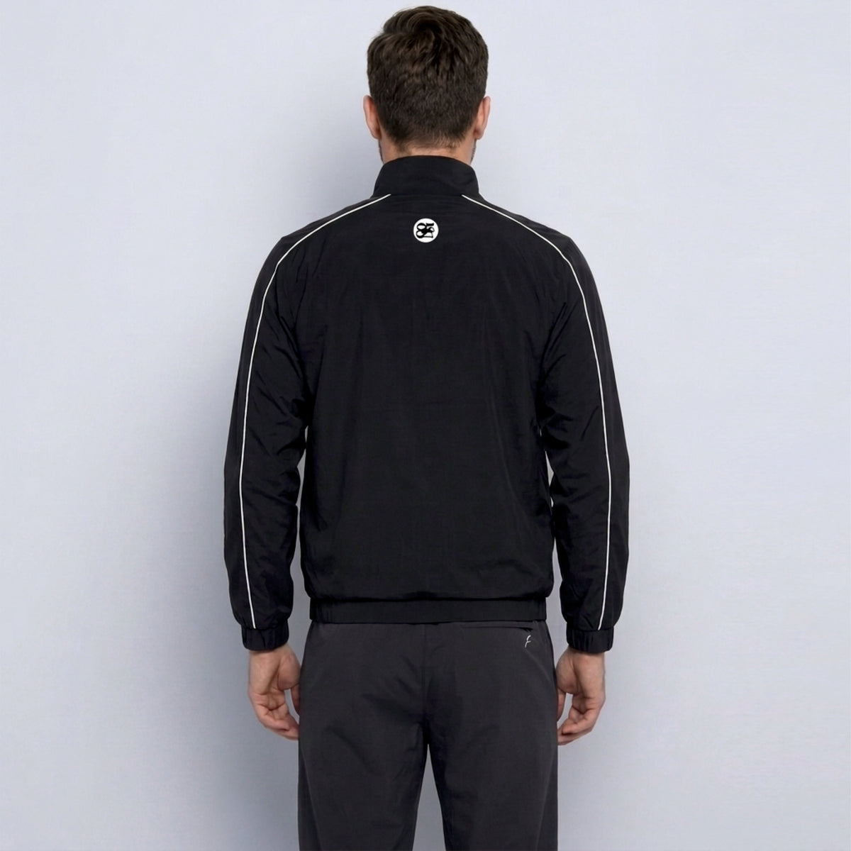 Person wearing a black tracksuit with a logo on the back against a white background