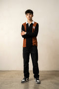 A long-sleeve rugby-style polo shirt with a color-blocked design featuring a rust brown body, black sleeves and center placket, and a white collar. A small circular logo is printed on the left chest.