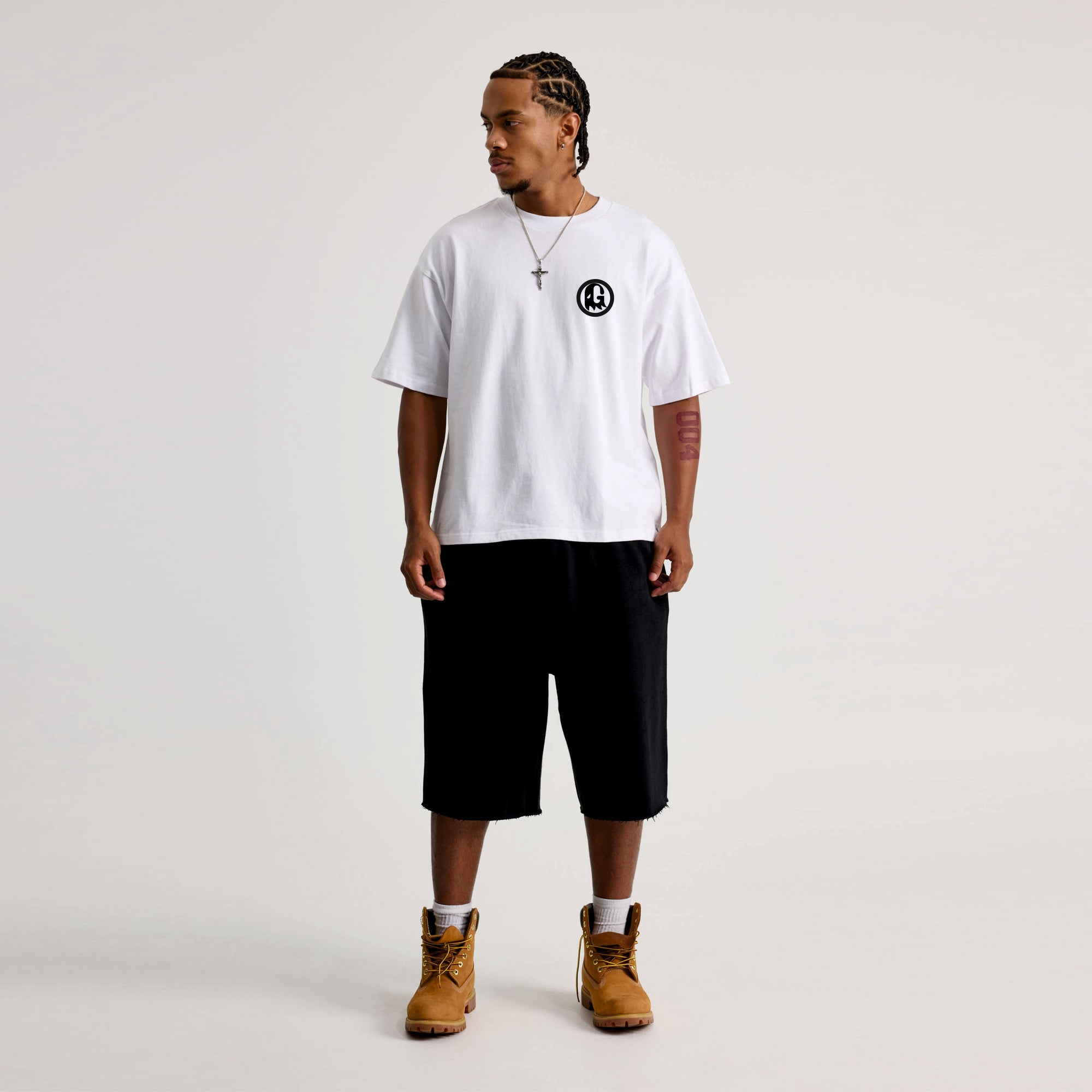 Person wearing a white t-shirt with a black logo, black shorts, and brown boots