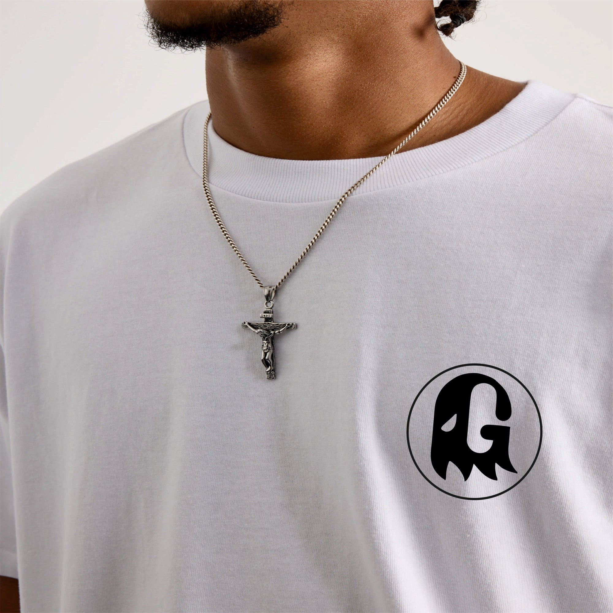 Person wearing a white t-shirt with a black logo and a necklace with a cross pendant.
