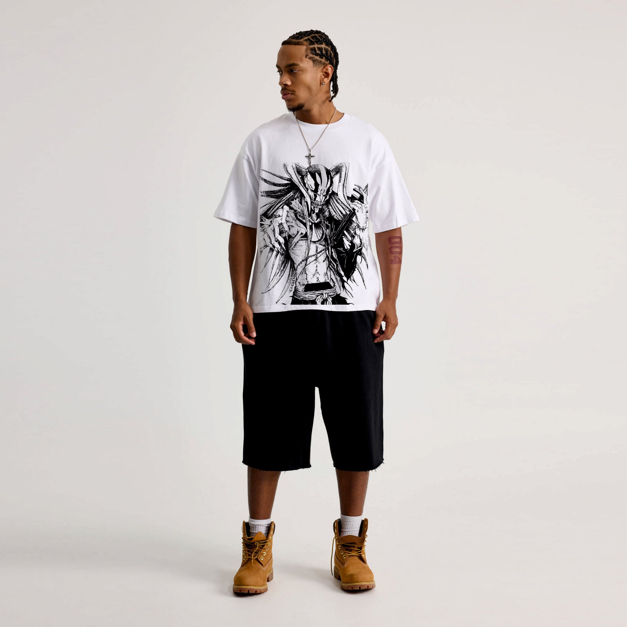Man wearing a white t-shirt with black graphic design, black shorts, and brown boots on a light gray background