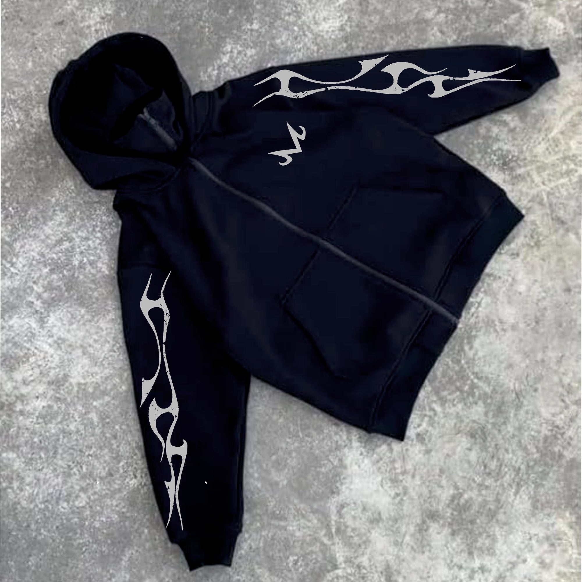 Black hoodie with white tribal designs on sleeves laid flat on a textured surface