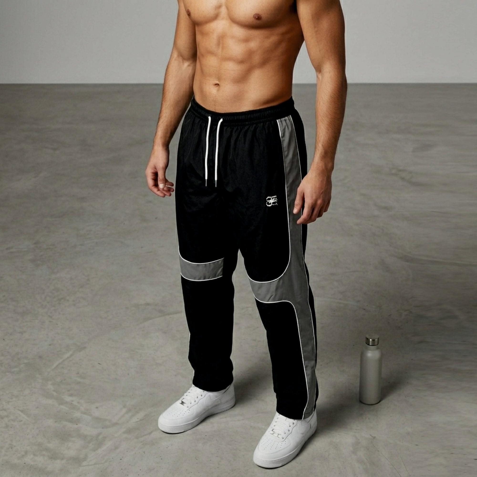 Man wearing black and gray track pants with a white bottle on a gray floor.