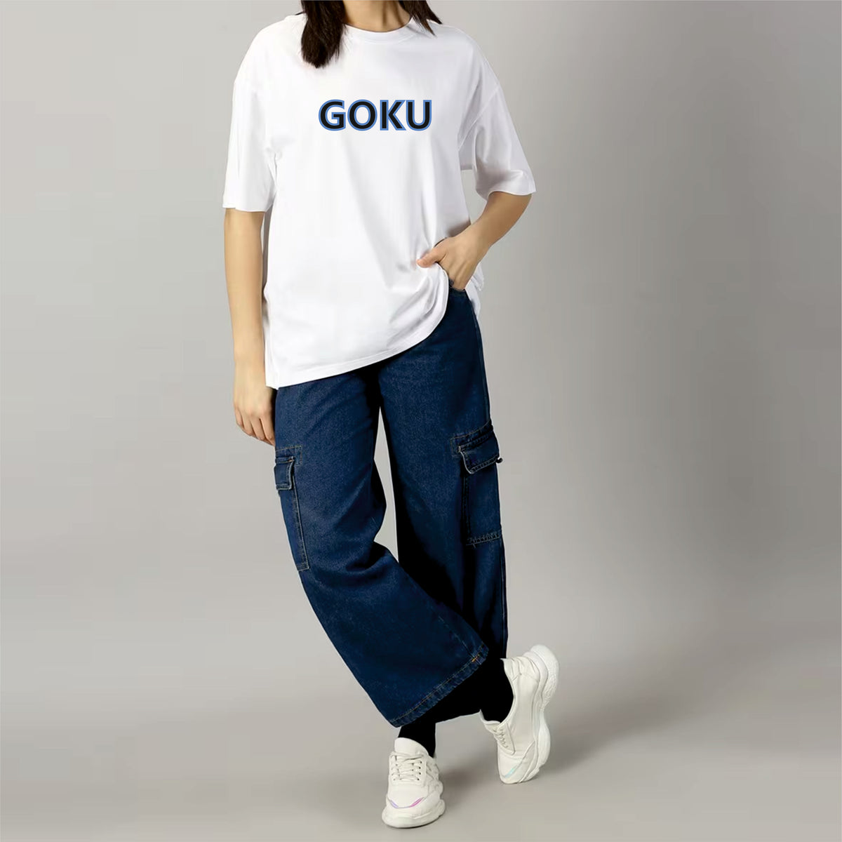 Person wearing a white t-shirt with 'GOKU' printed on it, blue jeans, and white sneakers against a gray background.