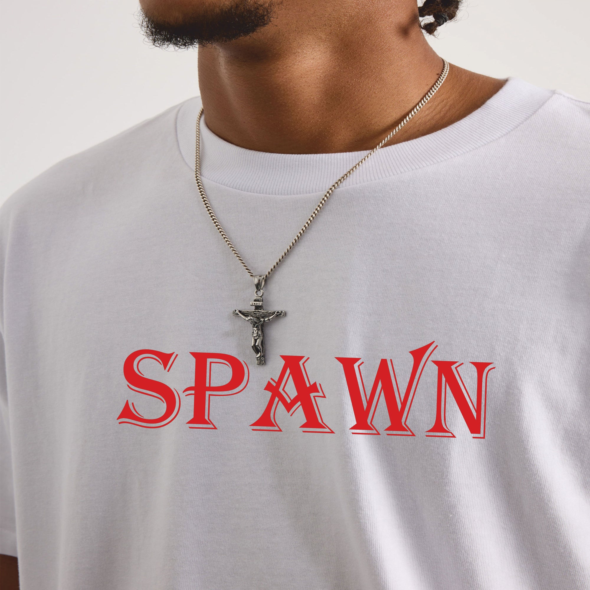Person wearing a white t-shirt with 'SPAWN' printed in red and a necklace with a cross pendant.