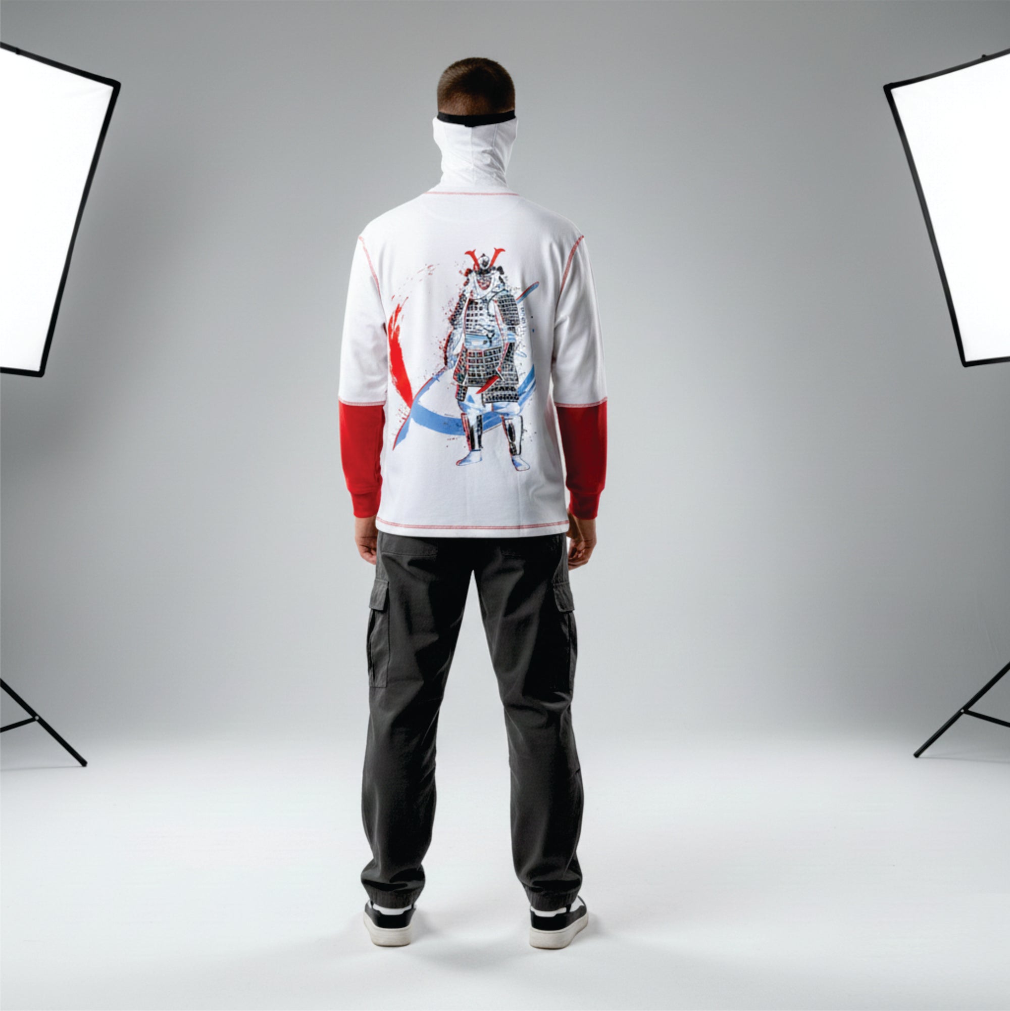 Person wearing a white hoodie with a graphic design on the back, standing in front of photography studio lights.