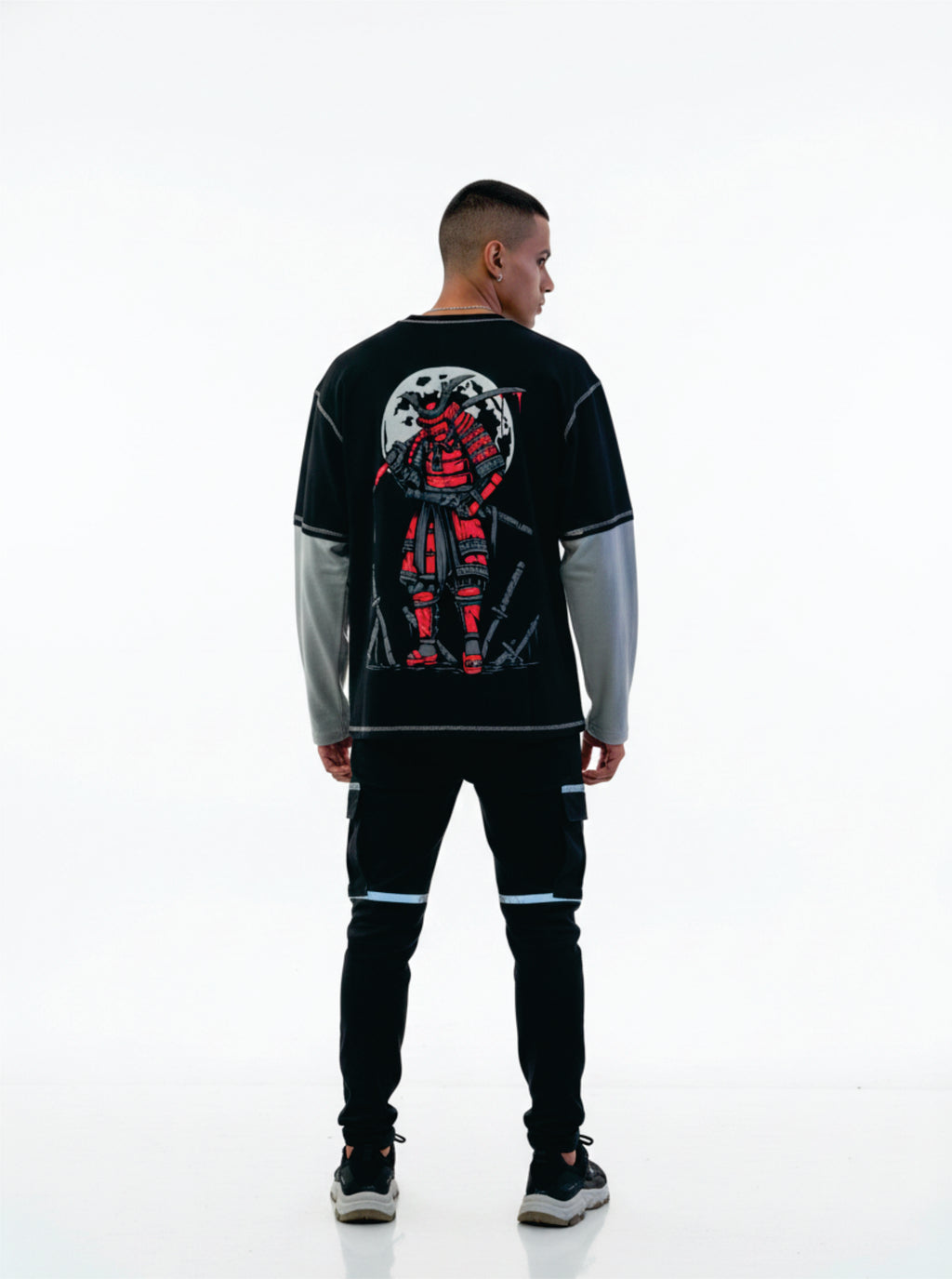 Person wearing a black and gray long-sleeve shirt with a red and white graphic on the back, standing against a white background.