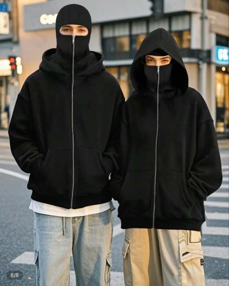 Two people wearing black hoodies with zippers on a city street.